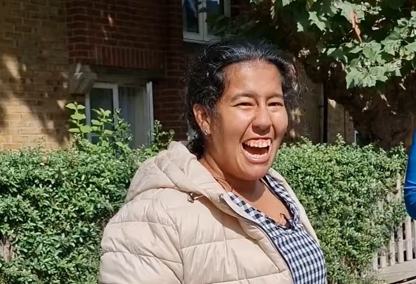 This photo is of Thalia. Thalia has a big smile on her face. She is wearing a blue and white gingham dress and a beige padded jacket.