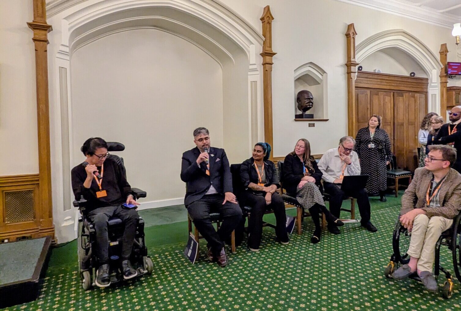 A group of people seated listening to a man speaking into a microphone