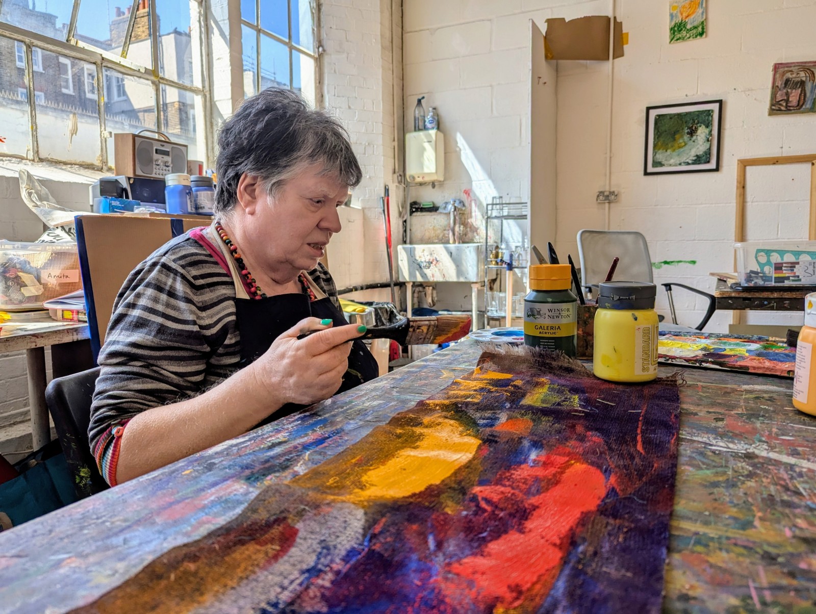 Person painting colourful artwork at a table in a bright art studio.