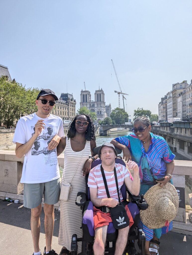 Group of four people posing on a bridge in Paris with Notre-Dame in the background.
