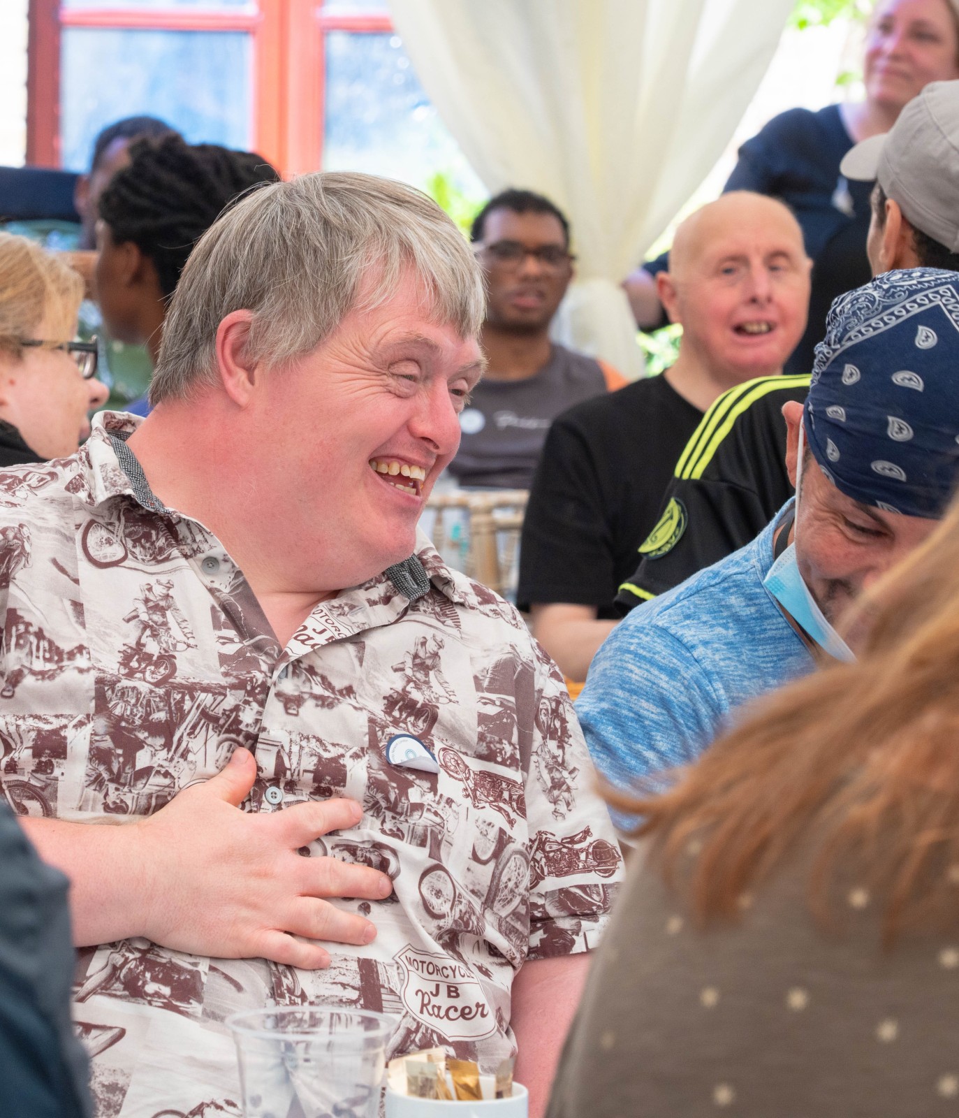 Man smiling while sitting and chatting with others at a table.