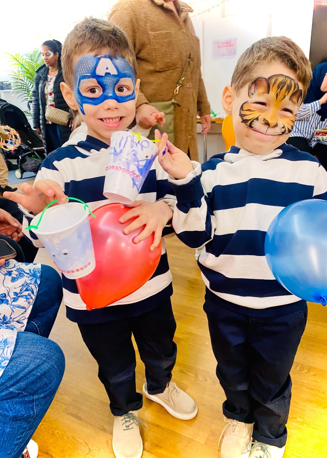 Two children with face paint holding balloons and craft cups at a family event.
