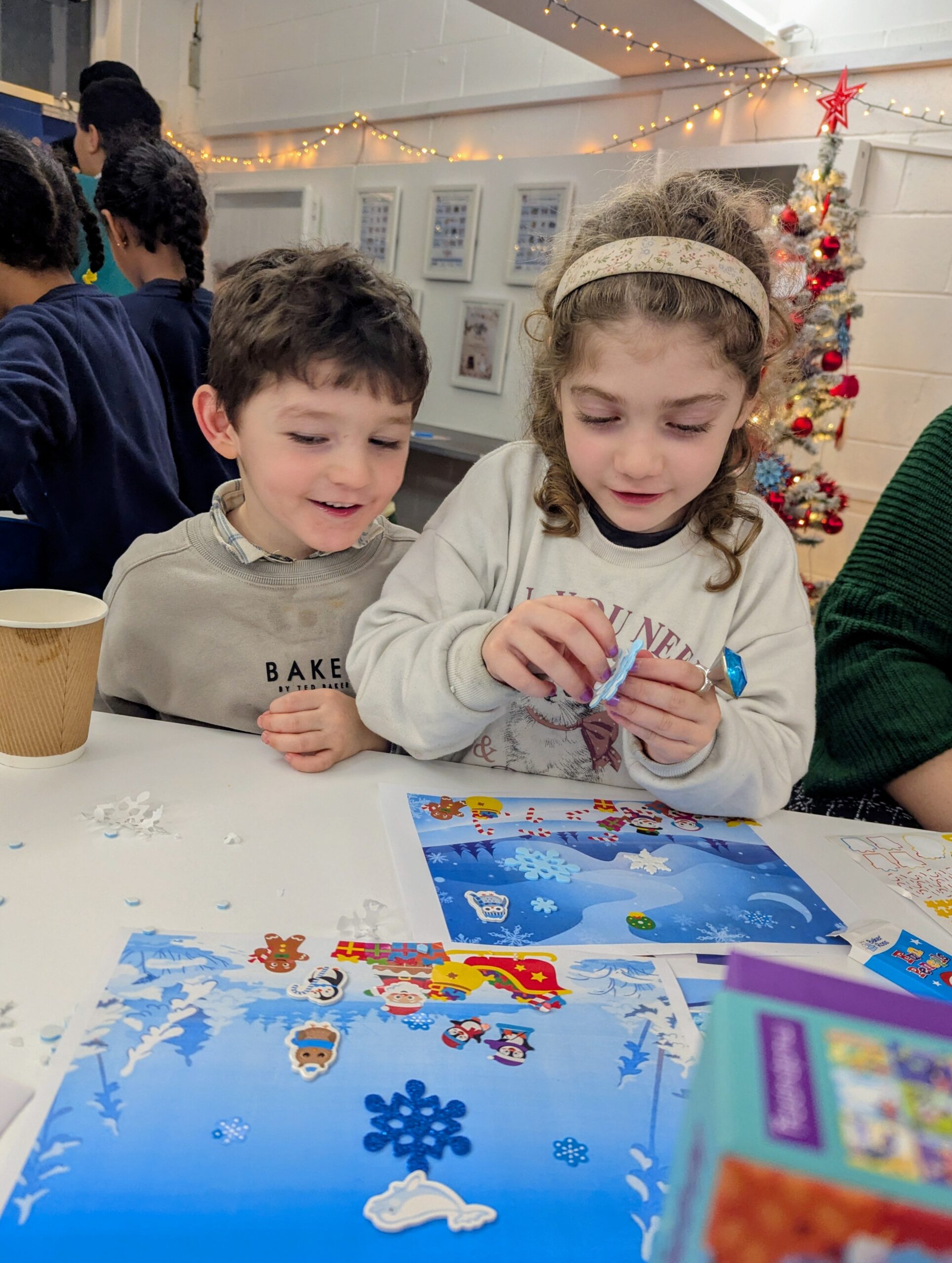 Children sitting at a table doing festive crafts with stickers.