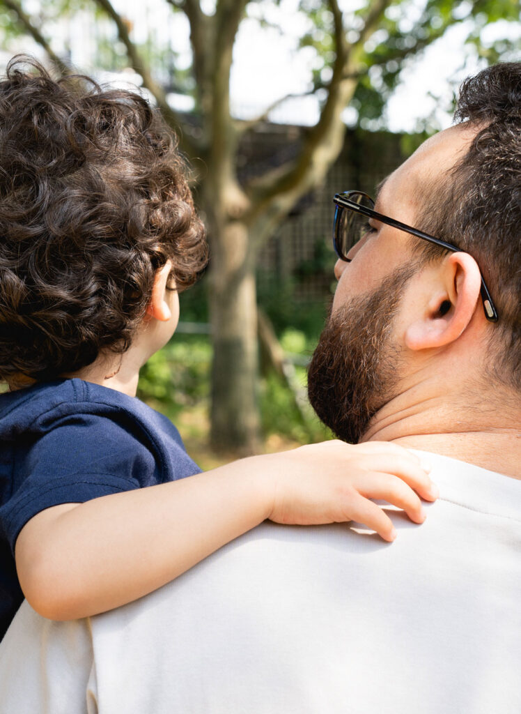Adult and child sitting together outdoors looking at trees.