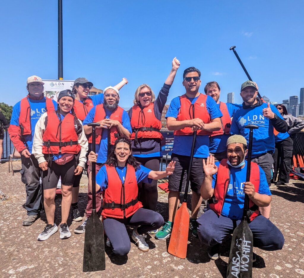 Group of people wearing life jackets holding paddles and celebrating by the water.