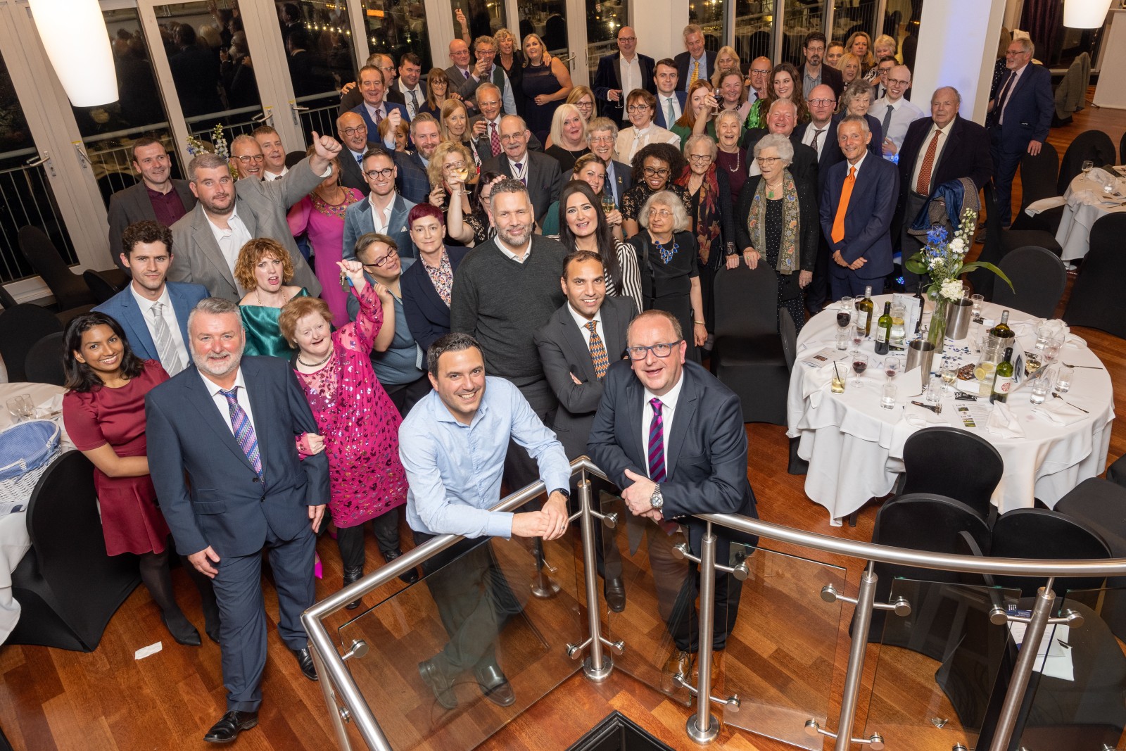 A large group of people stand and smile up at the camera