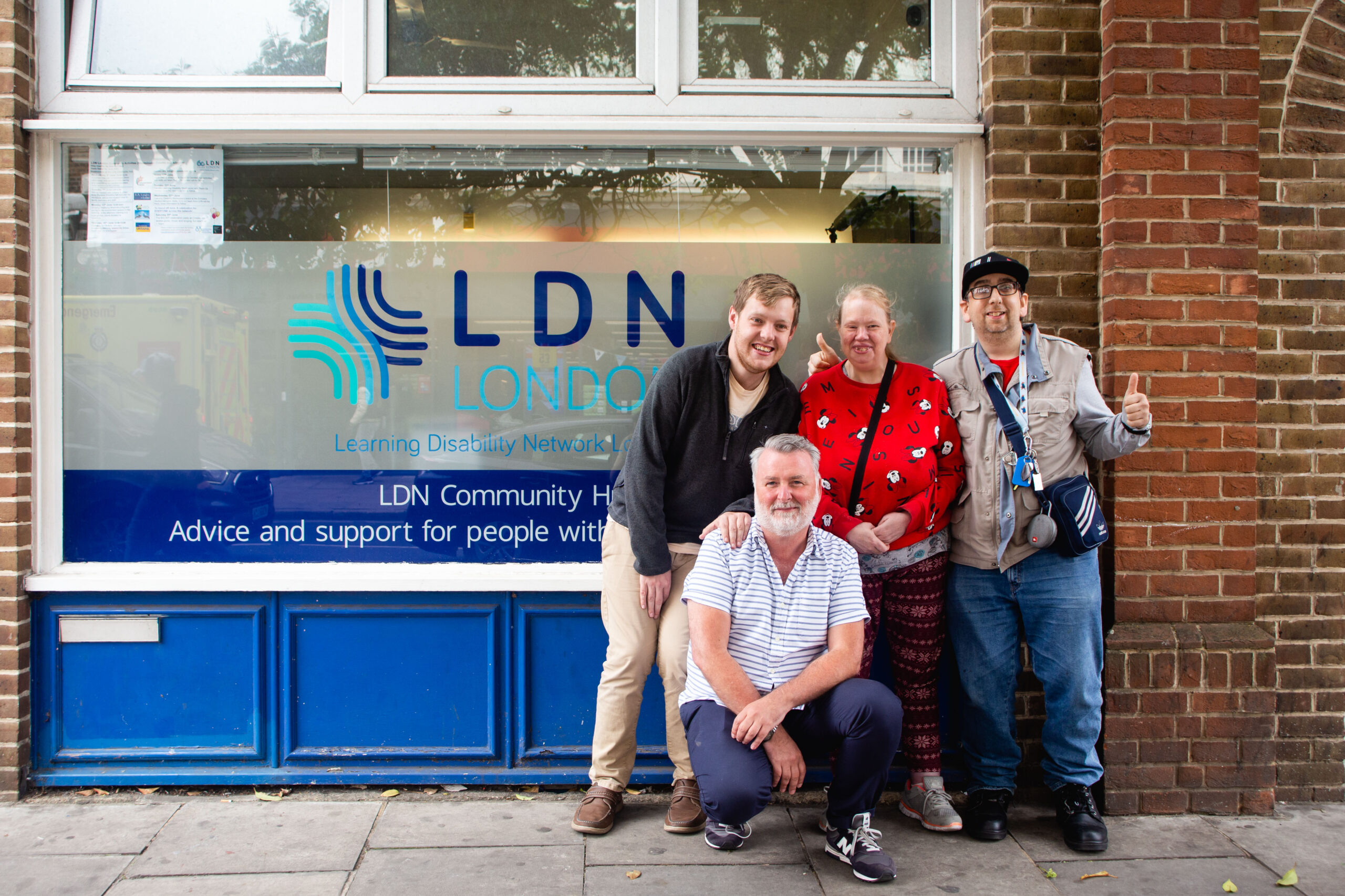 Four people smiling outside the LDN London community hub building.