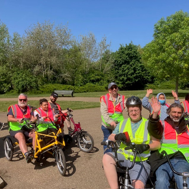 Group cycling adaptive bikes together in a park wearing high‑visibility vests.
