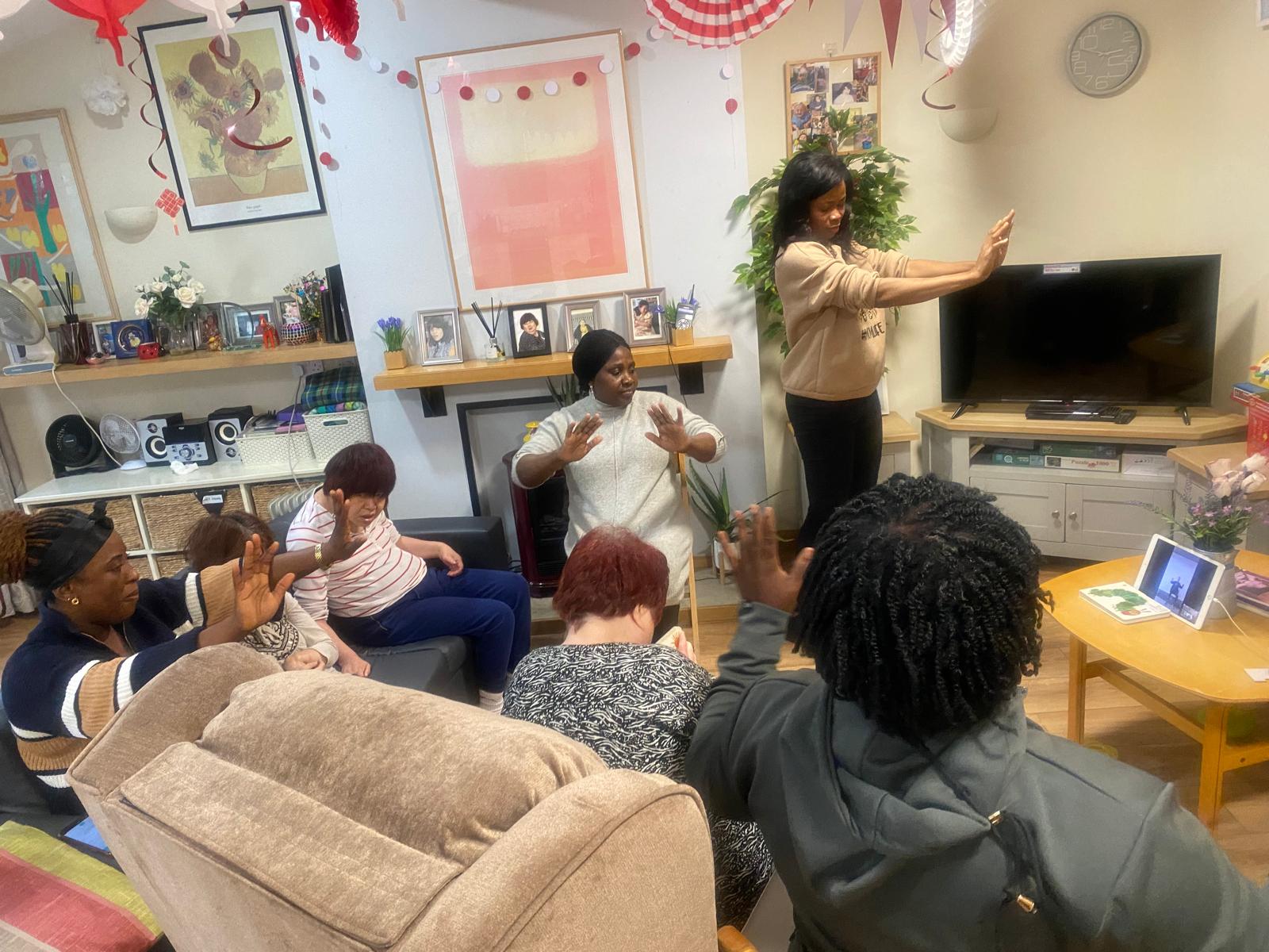 A group of people seated and standing looking at a screen on which someone is leading an exercise class