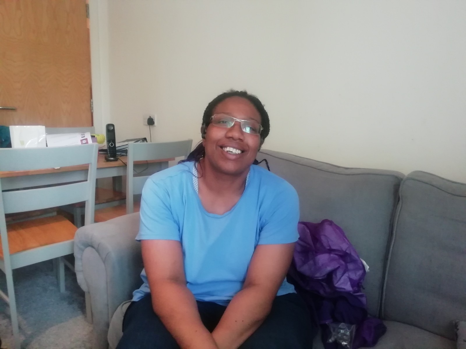 A woman is seated on her sofa smiling