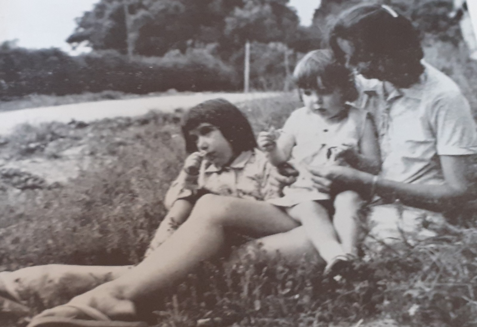 A mother and her two children are sitting on the grass