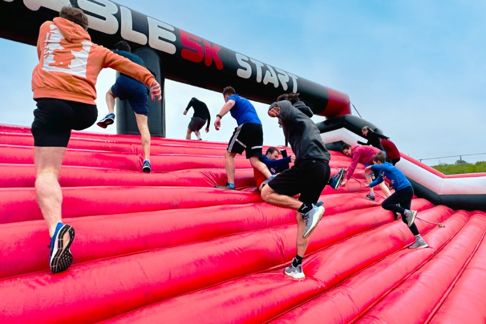 Participants climbing a large inflatable obstacle at an outdoor challenge event.