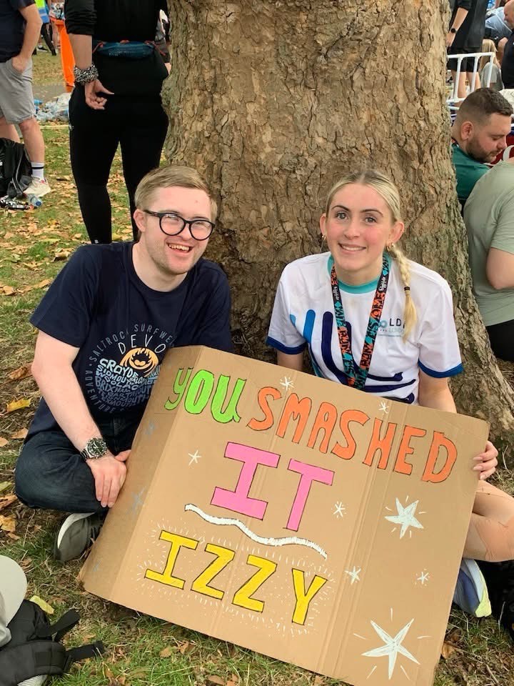 Two people sitting under a tree with a sign cheering on runners in the Big Half marathon