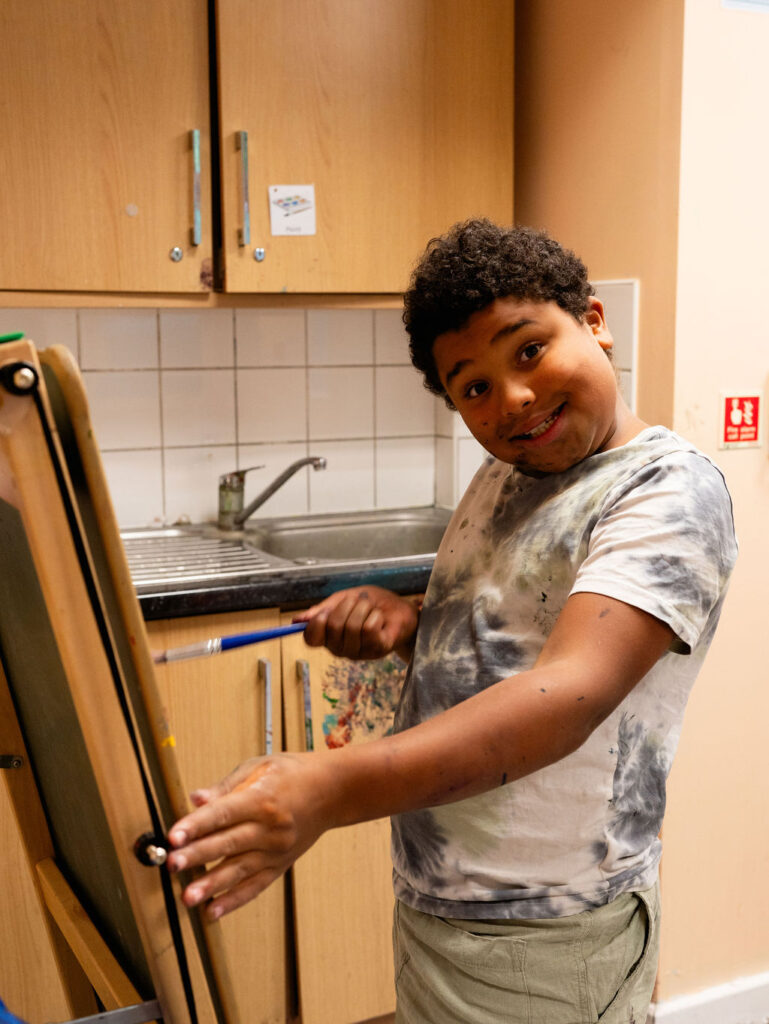 A young boy smiling while standing at an easel painting