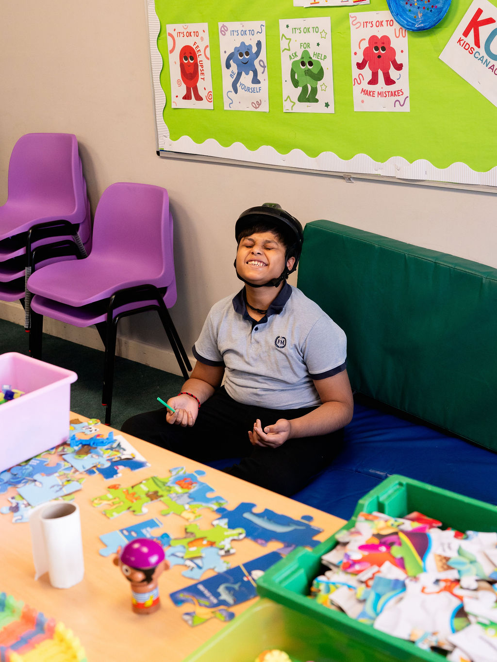 A young person sitting on the floor smileing with a table of activites in front of him
