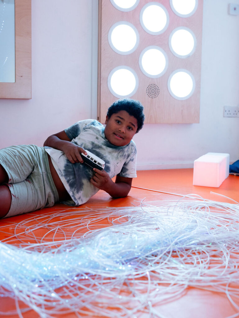 A young person lying on the floor playing in the sensory room at KCA