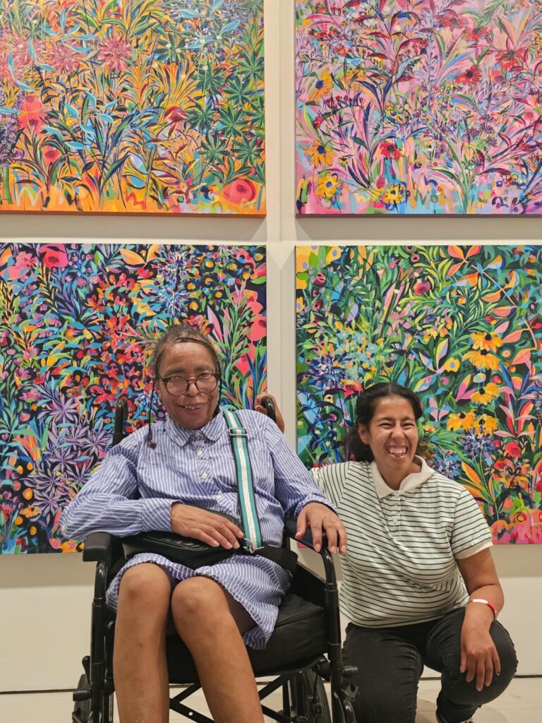 Two people smiling while sitting together in front of colourful artwork.