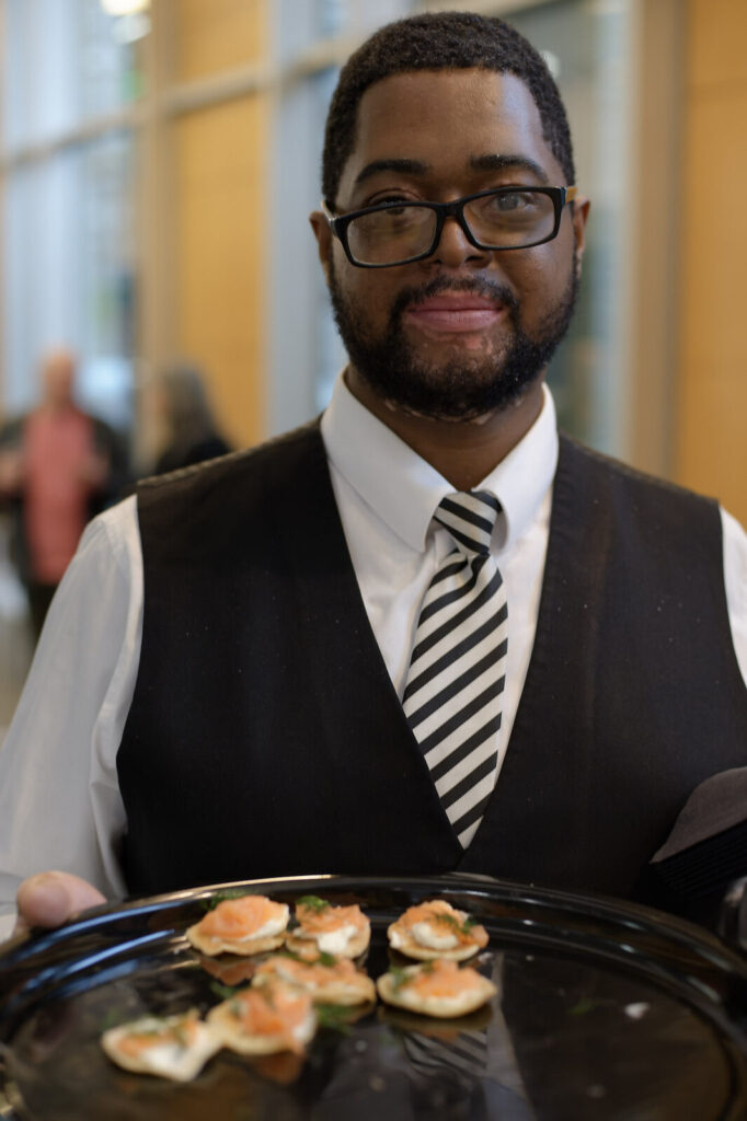 Server in formal uniform holding a tray of canapés.