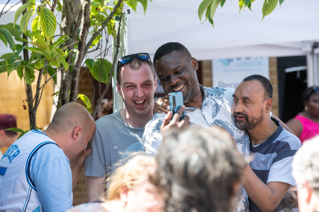 Group of people laughing together while looking at a phone at an outdoor community festival.
