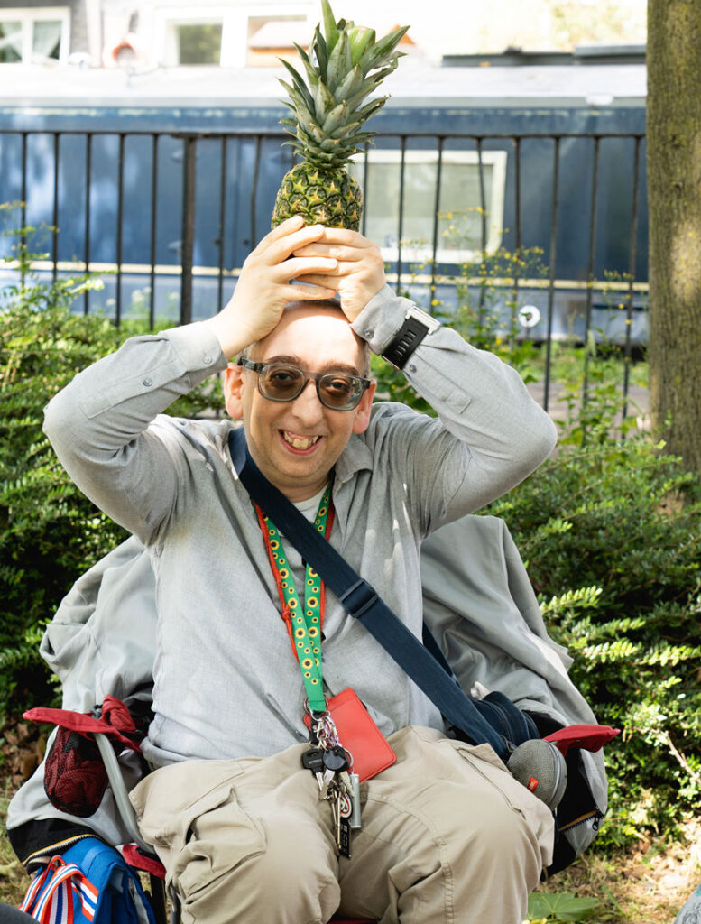 Man sitting outdoors holding a pineapple above his head and smiling playfully.