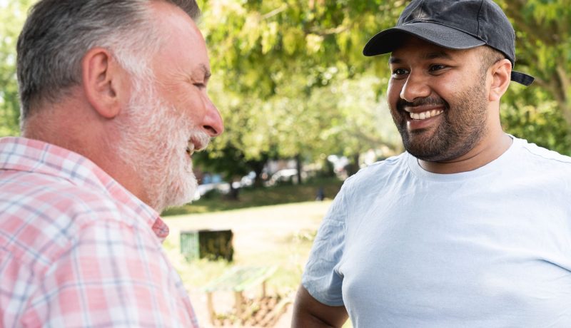 Two men smiling and chatting together outdoors in a park.