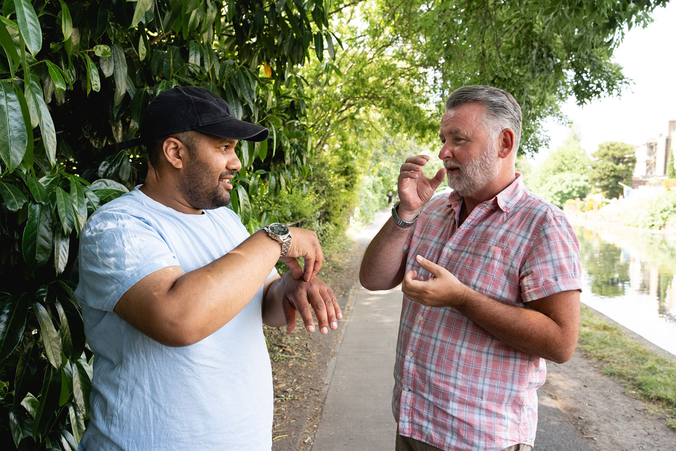 Two men chat to each other outside using Makaton