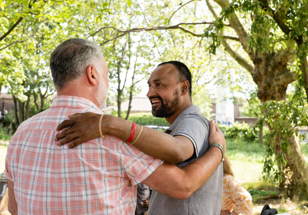 Two men smiling and embracing in a park setting.