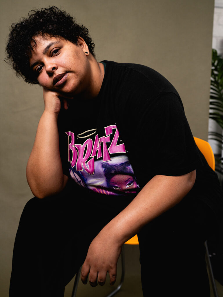 Portrait photo of a person sitting down looking at the camera with their arm resting on their knee