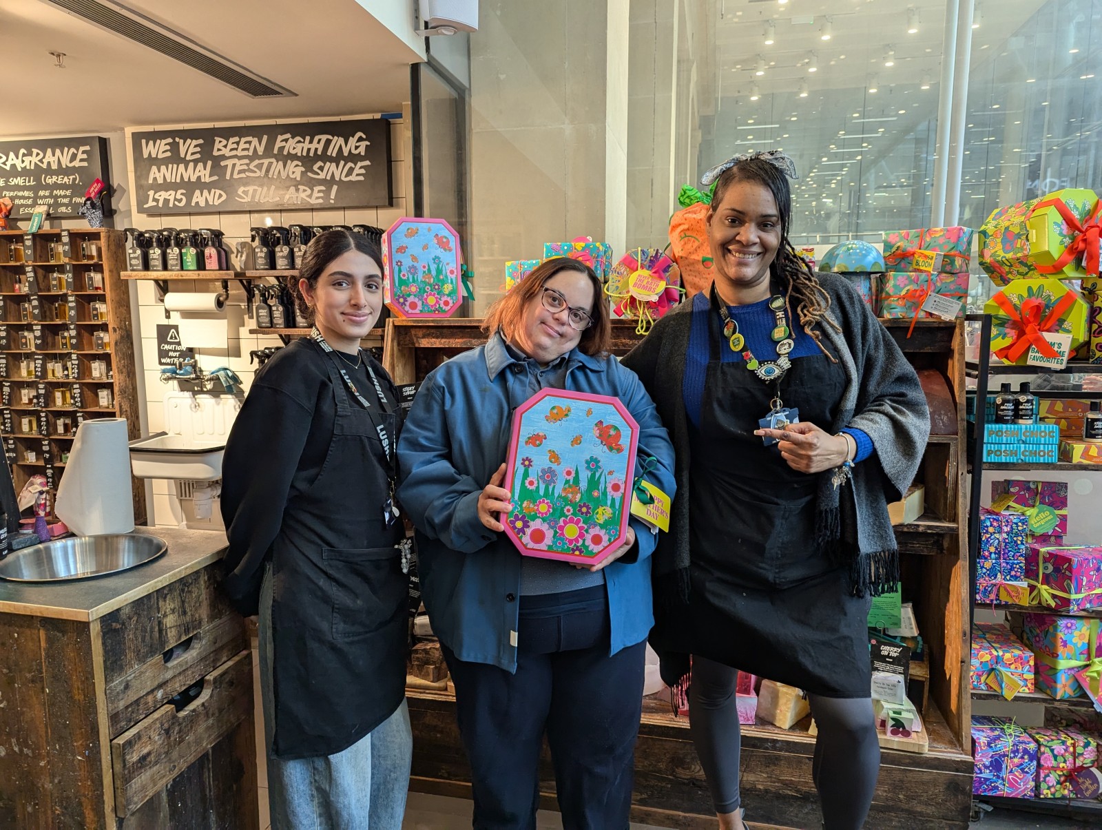 Three people standing together inside a colourful cosmetics shop showing artwork.