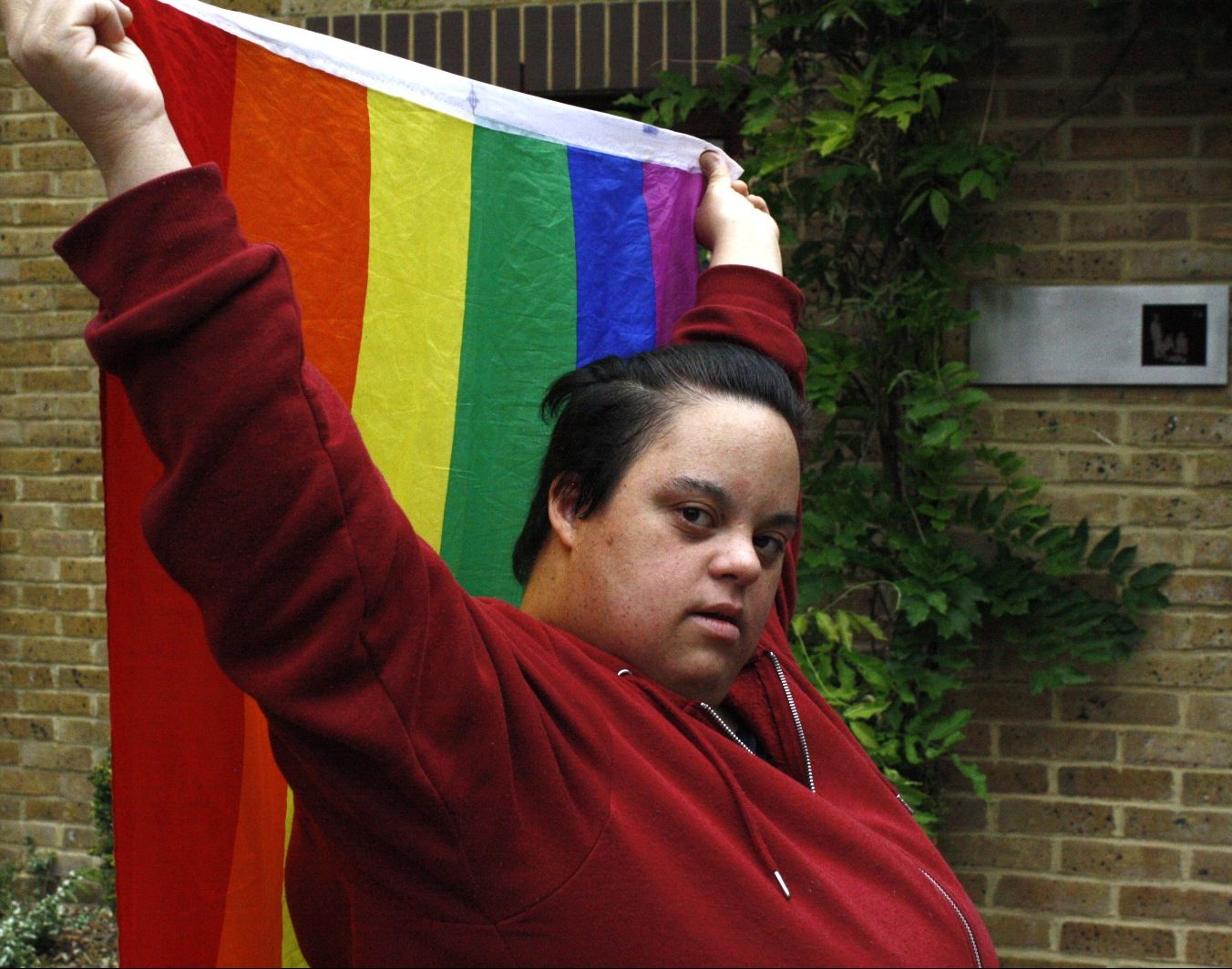 A woman holds a rainbow pride flag draped behind her