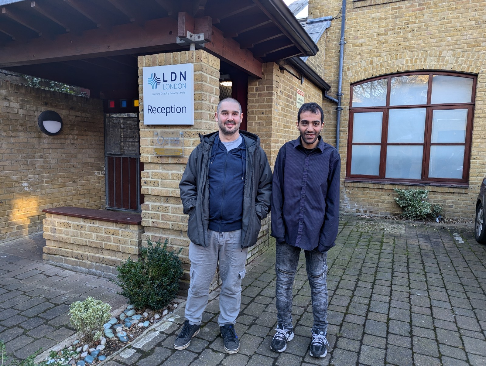 Two men stand outside the LDN London Reception building