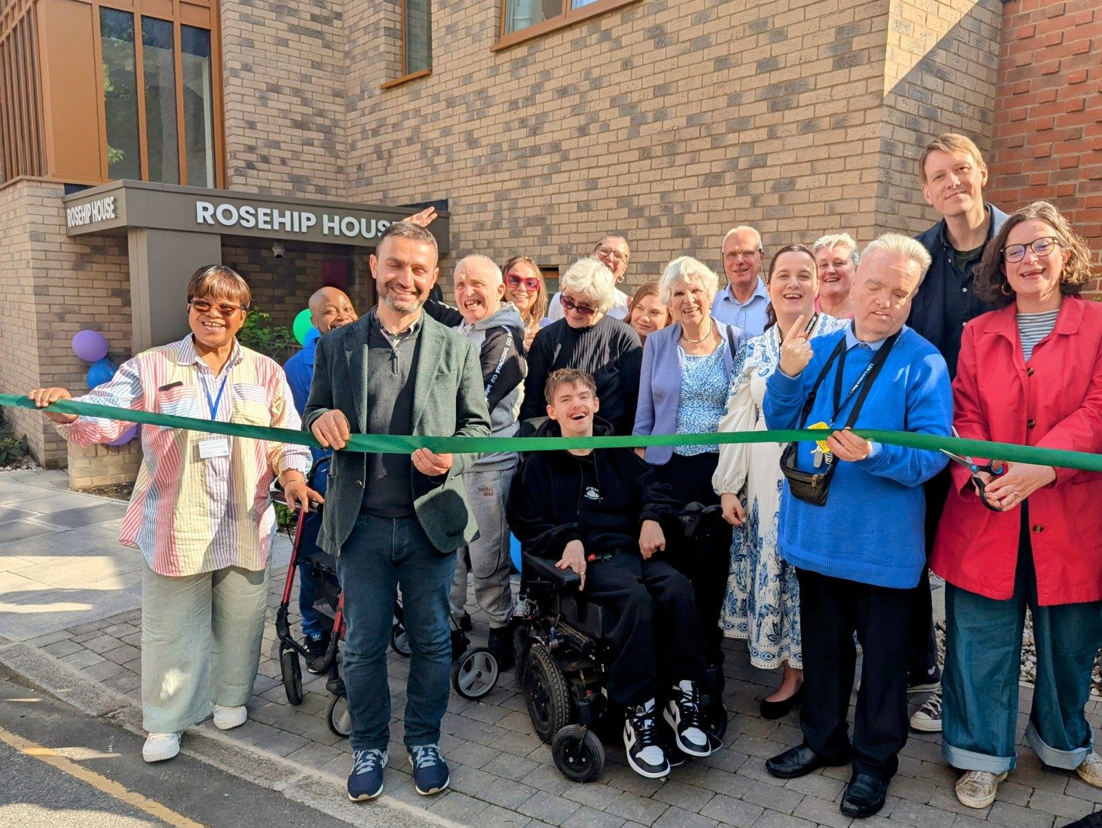 A group of people standing behind a ribbon outside a building saying Rosehip House