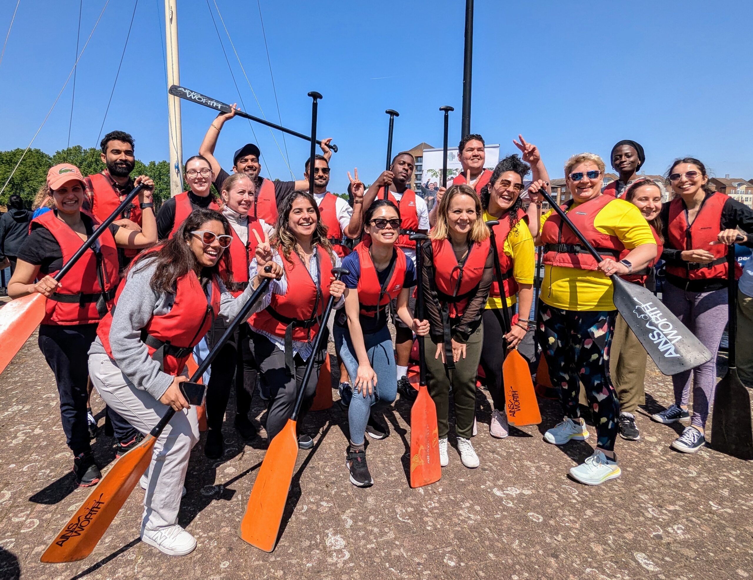 A team of people cheering, wearing lifejackets and holding oars