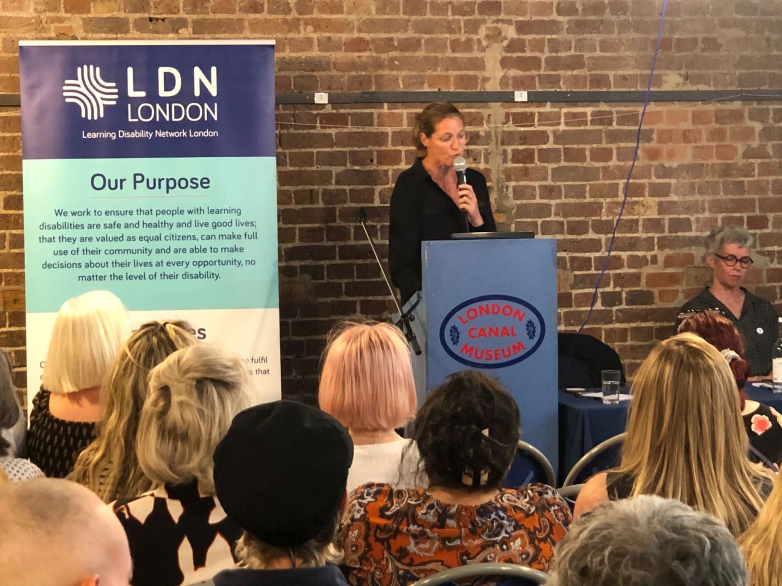 A group of people are sitting listening to a woman speak