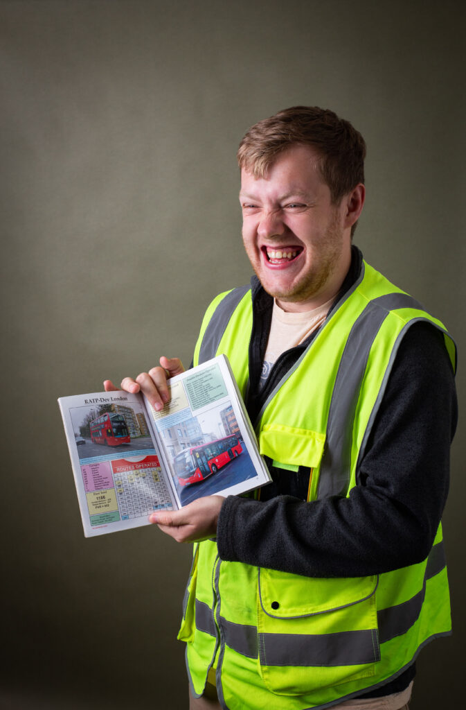 Man smiling and holding an open book showing images of buses.