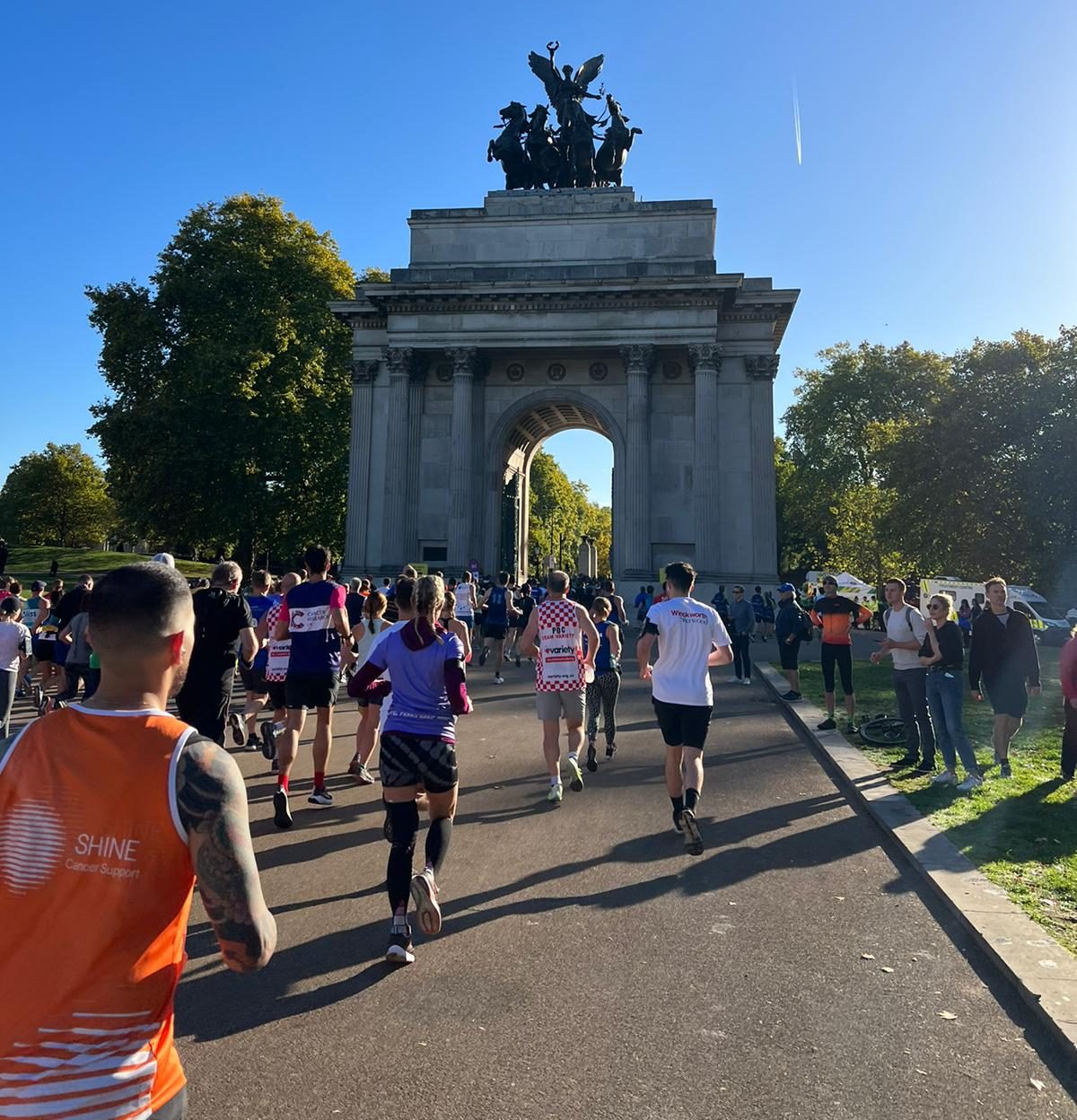Runners taking part in a road race through a park with spectators watching.