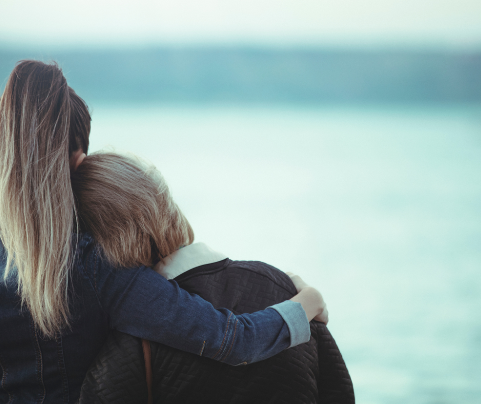 Two people with their backs to the camera, one has her arm around the other