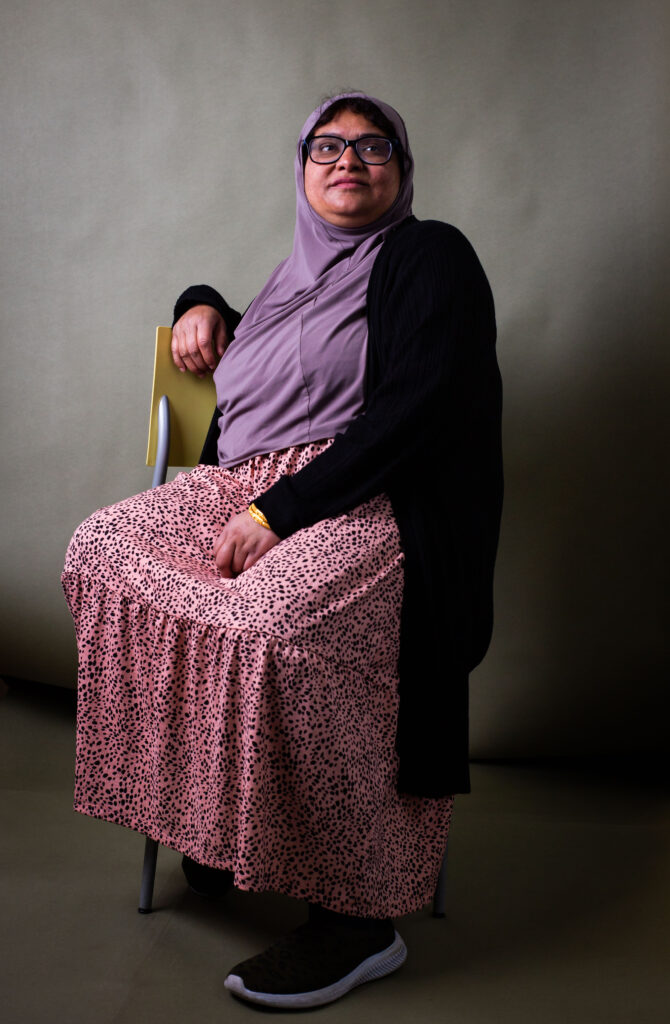 Woman wearing a headscarf sitting on a chair and looking to the side in a studio portrait.