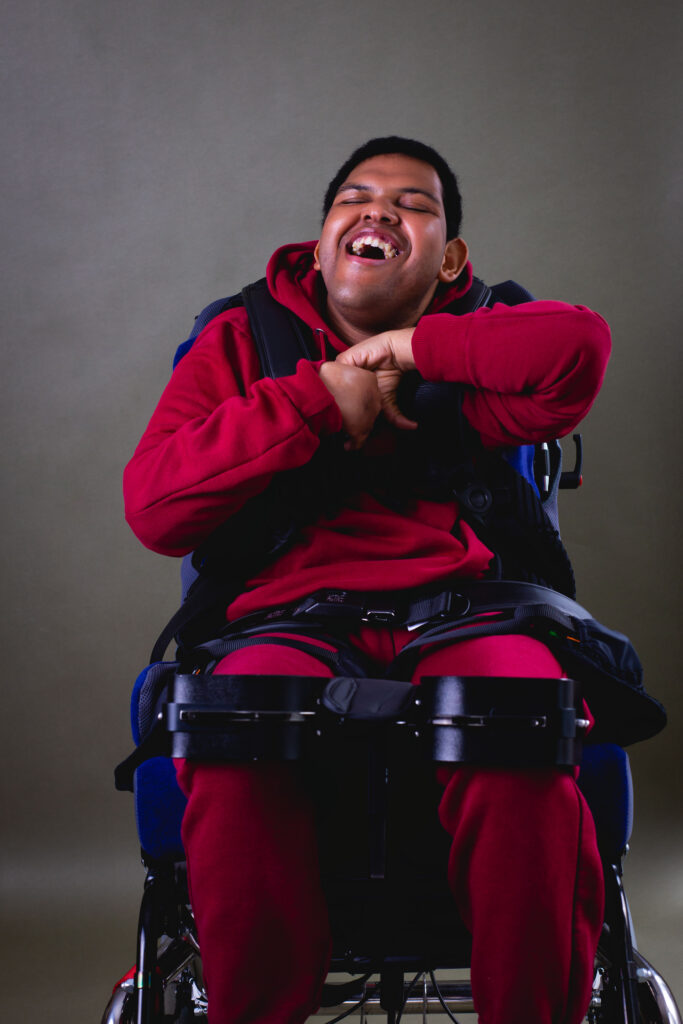 Young man in a wheelchair smiling with his eyes closed and hands together in a joyful pose.