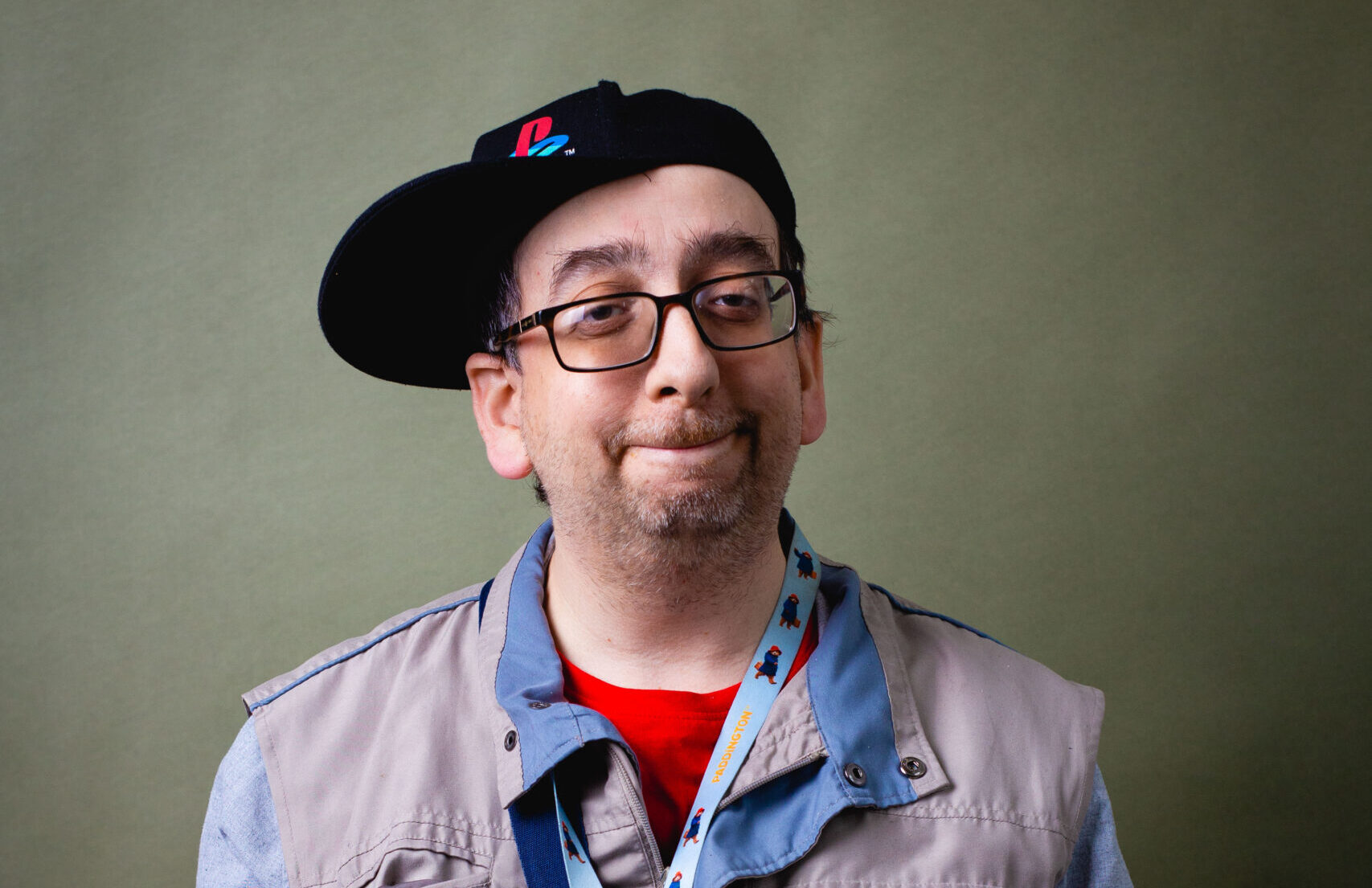Man wearing a cap and glasses sitting for a studio portrait with a neutral expression.