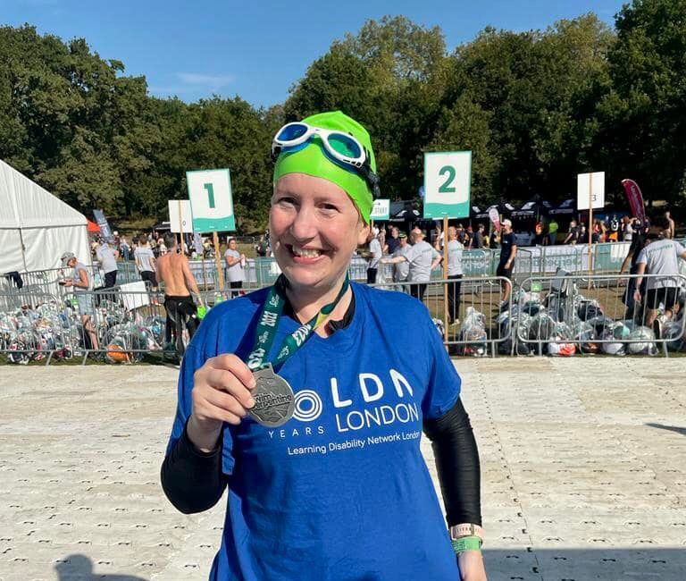 Smiling participant wearing an LDN London t-shirt holding up a medal after completing an event.