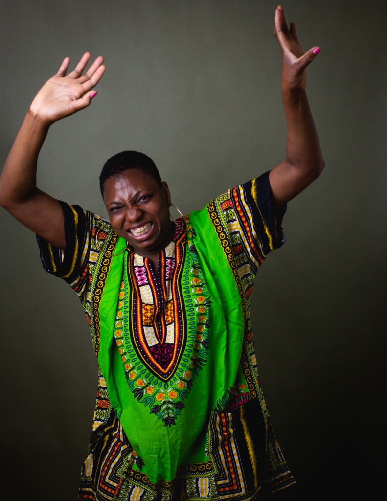 Woman wearing a bright patterned top raising her arms and smiling in a studio portrait.