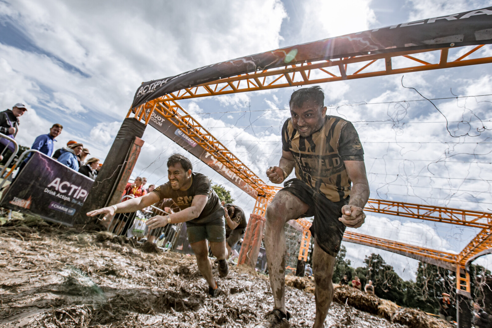 Participants crawling through mud under a net obstacle during a Tough Mudder challenge.