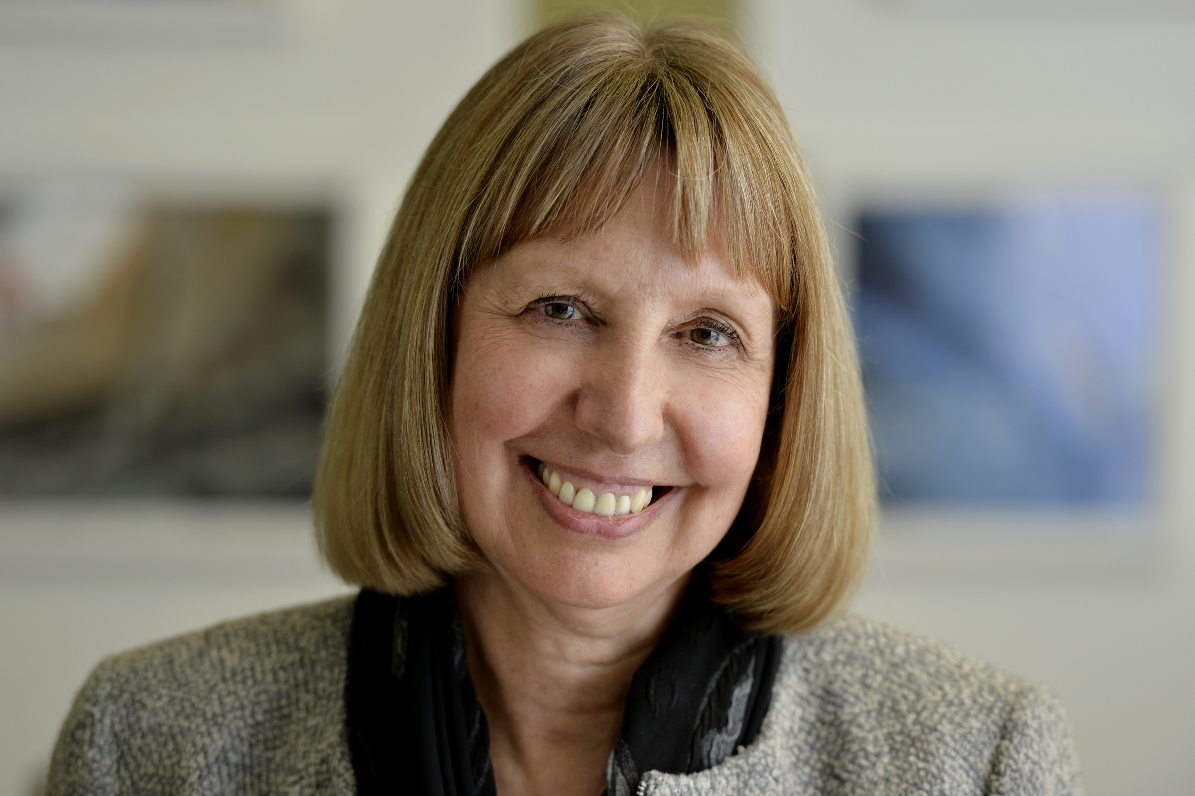 A high quality photo of a middle aged woman with a blonde / brown bob haircut and dressed professionally. She has a large smile.