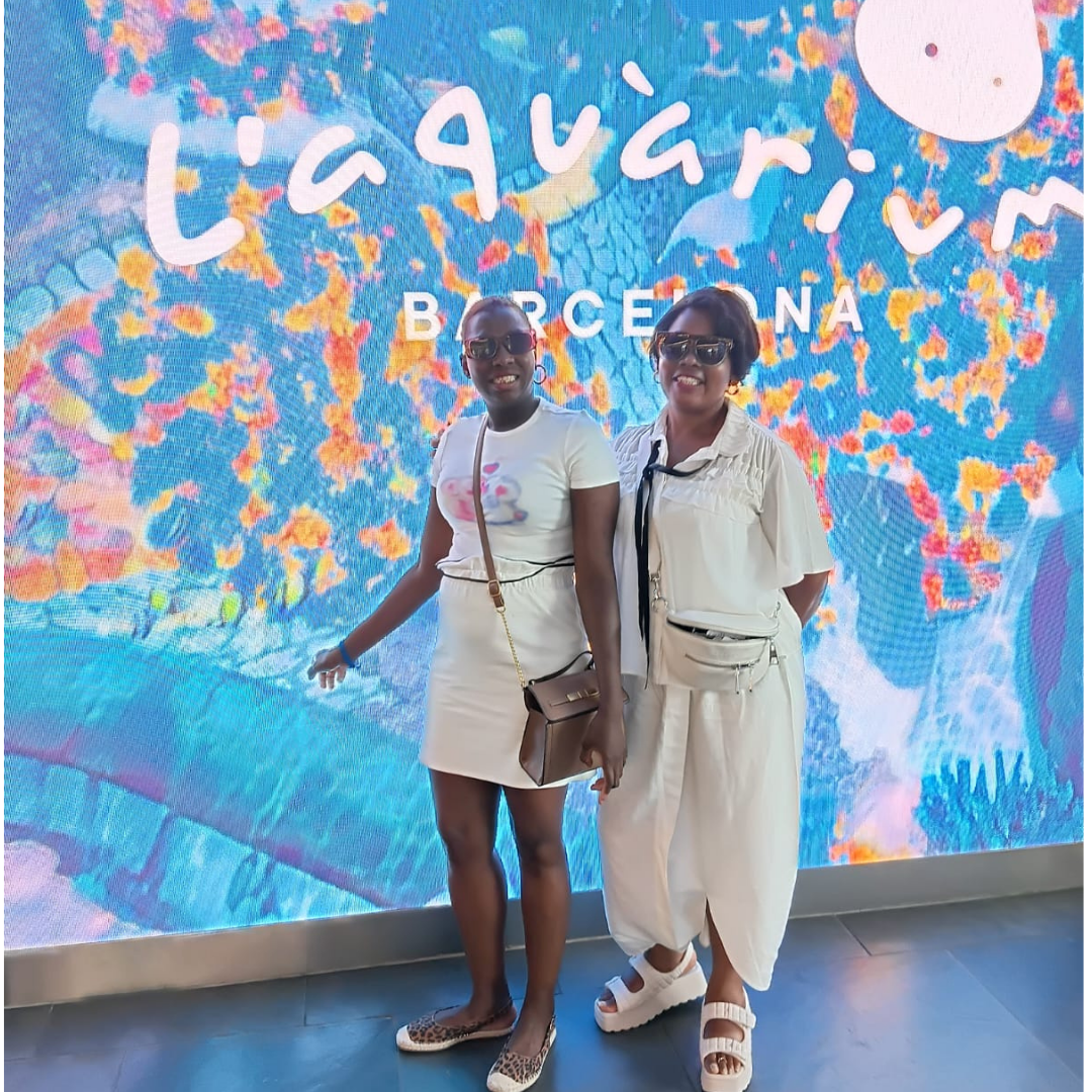 Two women are posing in front of a screen with a blue coloured background, which says 'L'aquarium' Barcelona on it.